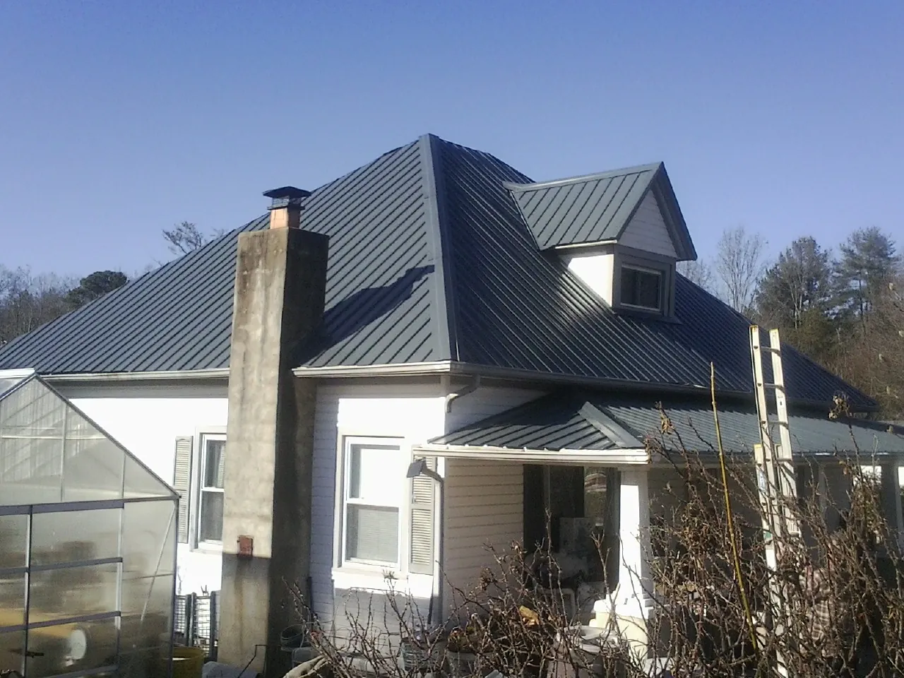Dark blue standing seam metal roof on a white farmhouse with dormer — Slate & Tile Roof Repair by Roofing Brothers in Green