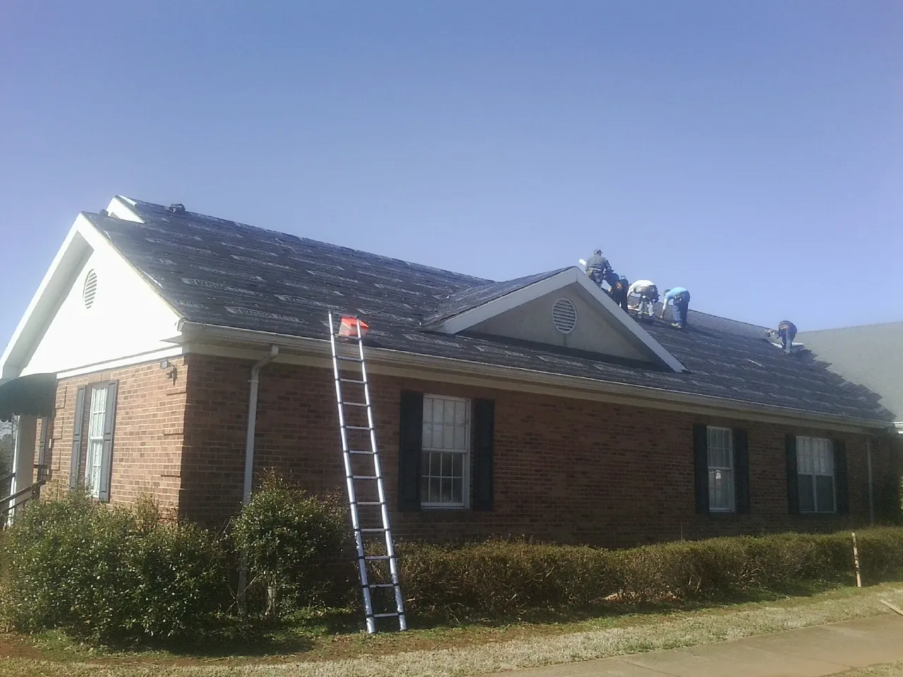 Crew tearing shingles off a brick ranch roof with a ladder set — Emergency Roof Repair work by our crew in Green