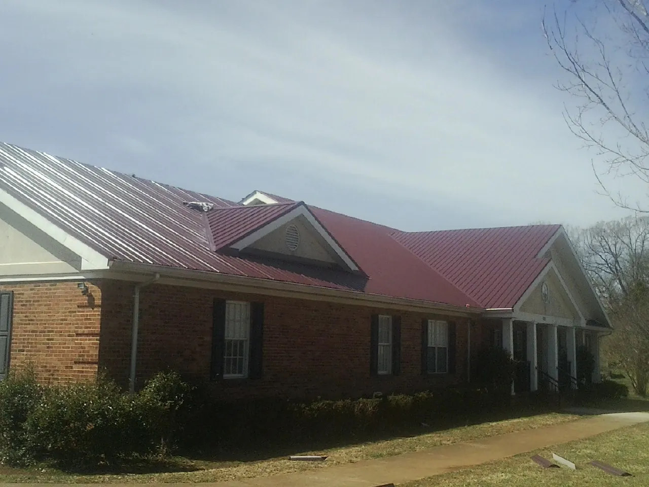 Red metal roof with gabled entries on a long brick building, from a Hail Damage Roof Repair job in Green