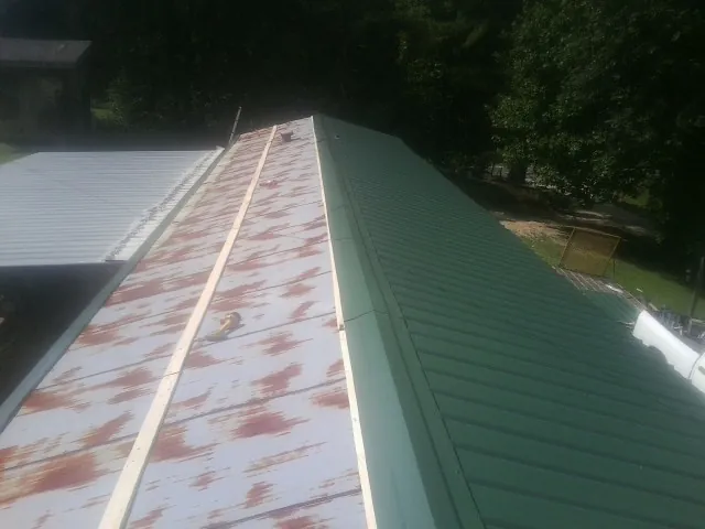 Old rusted panels beside newly installed green metal roofing — Wind Damage Roof Repair by Roofing Brothers in Green