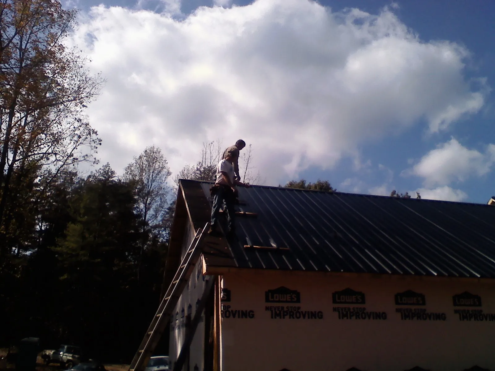 Roofer fastening dark metal panels high against a cloudy sky, from a Roof Inspection job in Green