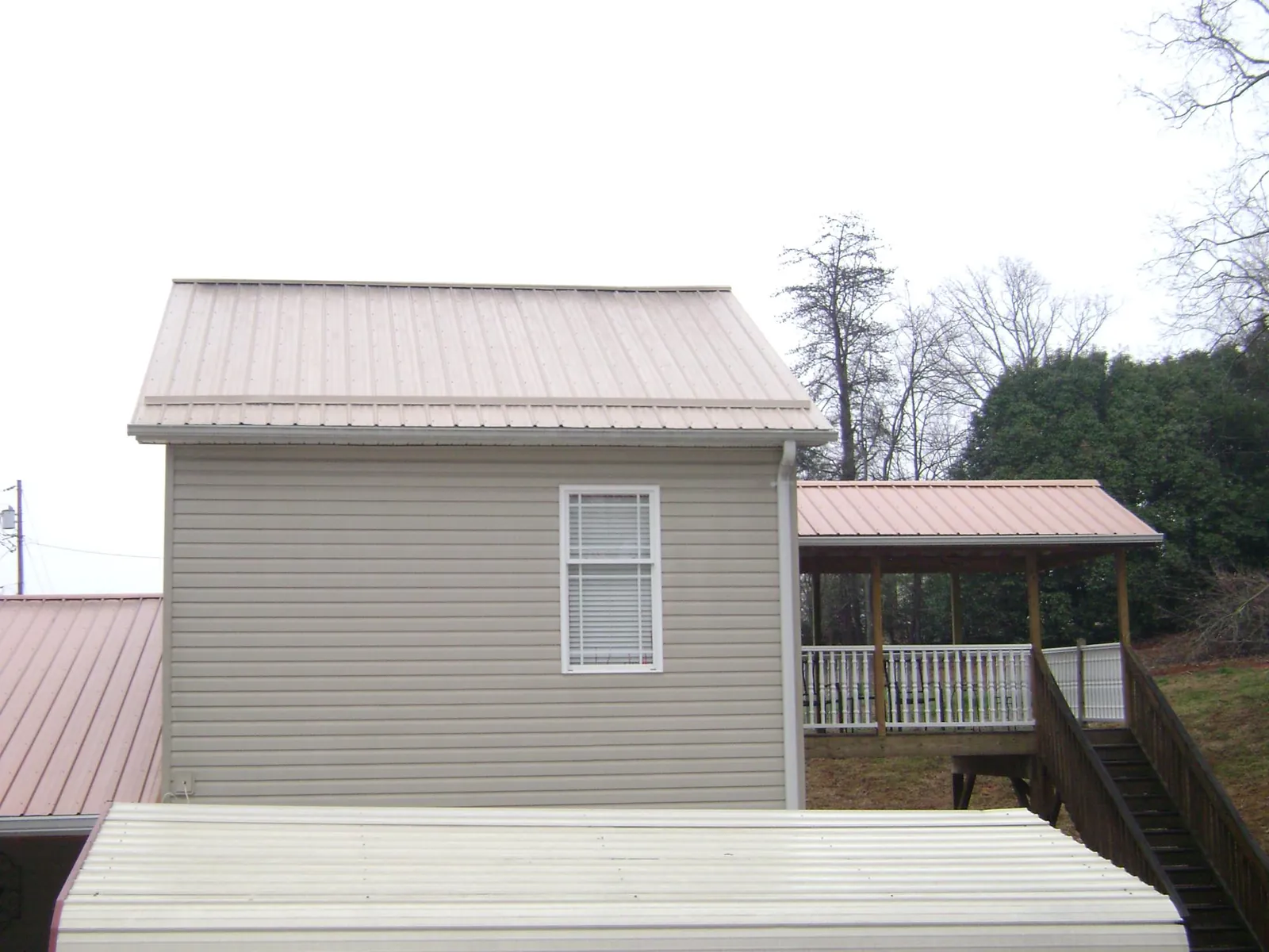 Tan metal roofs on a two story addition and attached porch, from a Roof Replacement job in Green